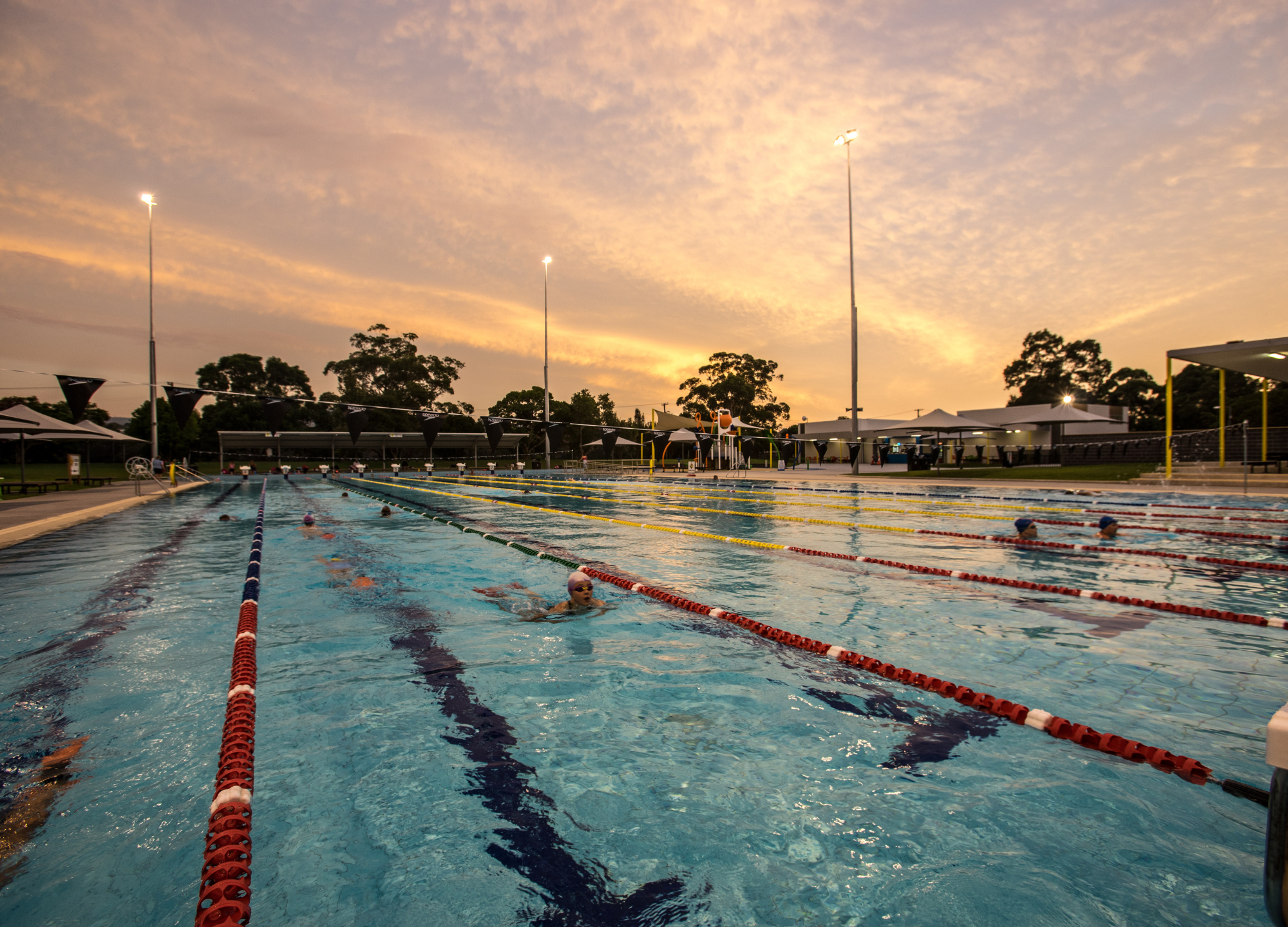 A photo of the pool at Nowra Aquatic Park with people swimming in it at dusk