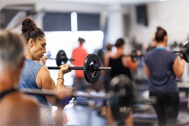 Patron lifting a barbell as part of group fitness class in group fitness studio